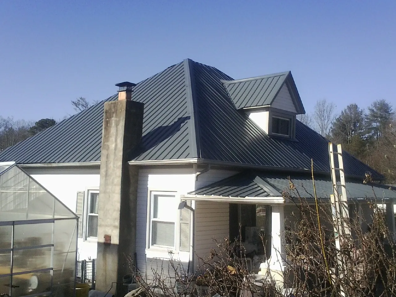 Dark blue standing seam metal roof on a white farmhouse with dormer — Slate & Tile Roof Repair by Roofing Brothers in Swansboro