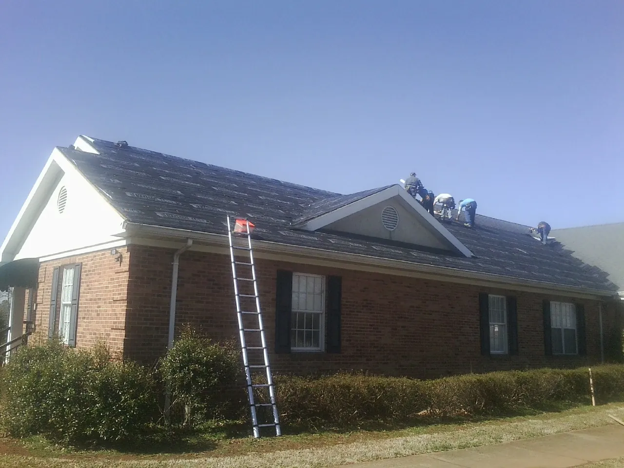 Crew tearing shingles off a brick ranch roof with a ladder set — Emergency Roof Repair work by our crew in Swansboro