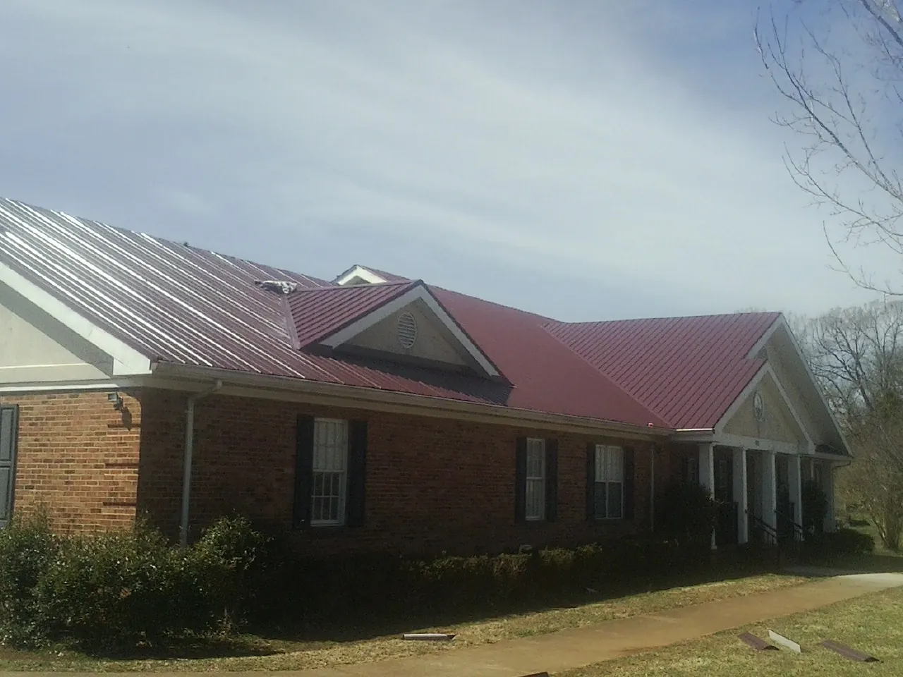 Red metal roof with gabled entries on a long brick building, from a Hail Damage Roof Repair job in Swansboro