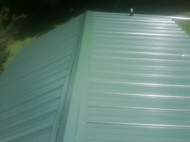 New green metal panels meeting at the ridge of a roof — Flat Roof Repair work by our crew in Swansboro