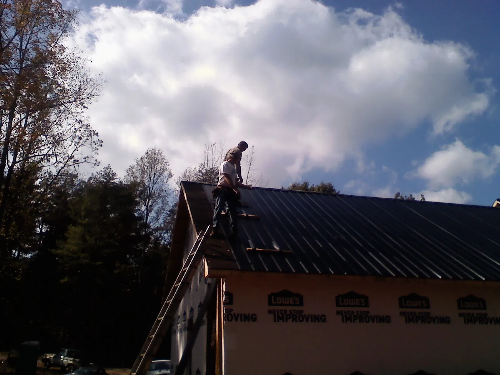 Roofer fastening dark metal panels high against a cloudy sky, from a Roof Inspection job in Swansboro