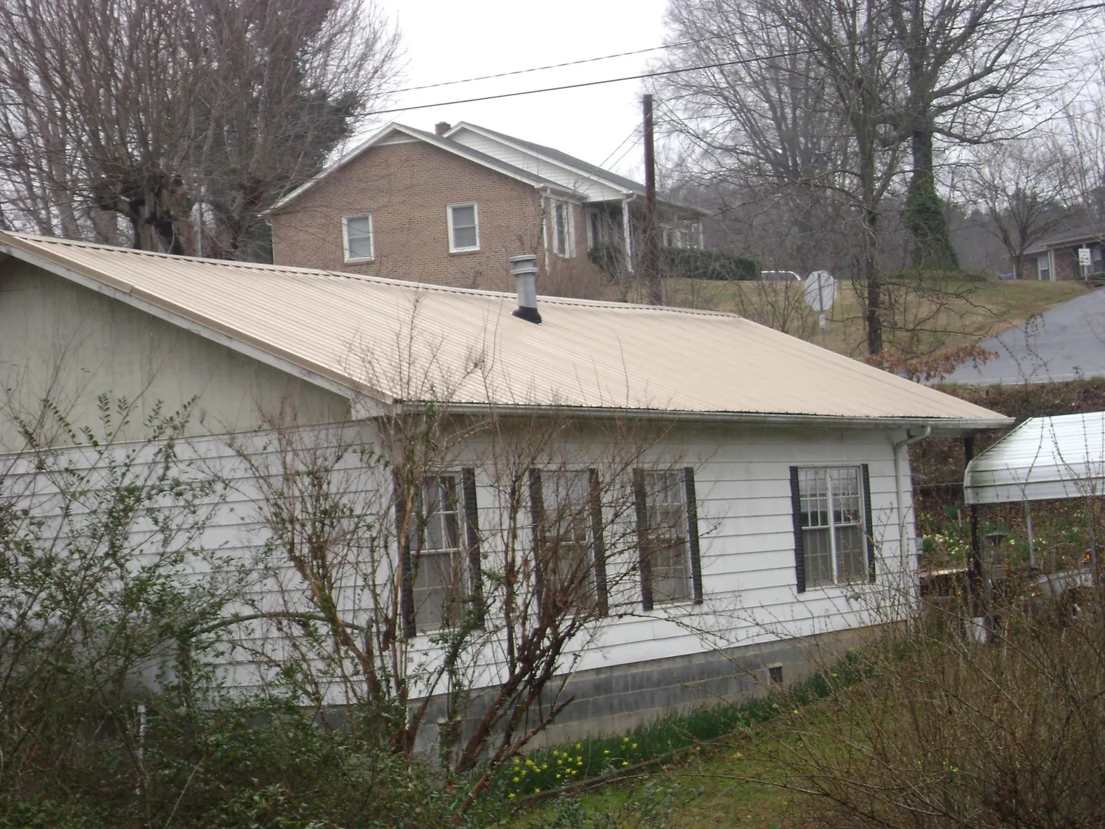 Tan metal roof on a white sided house set into a hillside — Commercial Roofing by Roofing Brothers in Swansboro